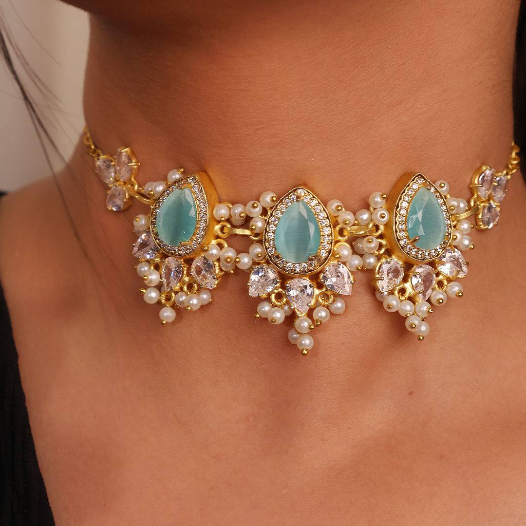 Close-up of a gold necklace with turquoise stones and pearl accents on a person wearing a black top.