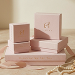 Load image into Gallery viewer, Stack of pink jewelry boxes with 'Auricka' branding on a wooden surface.
