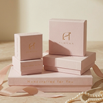 Load image into Gallery viewer, Stack of pink jewelry boxes with 'Auricka' branding on a wooden surface.