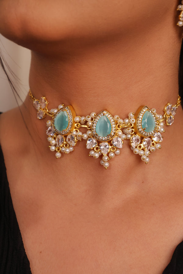 Close-up of a gold necklace with turquoise stones and pearl accents on a person wearing a black top.