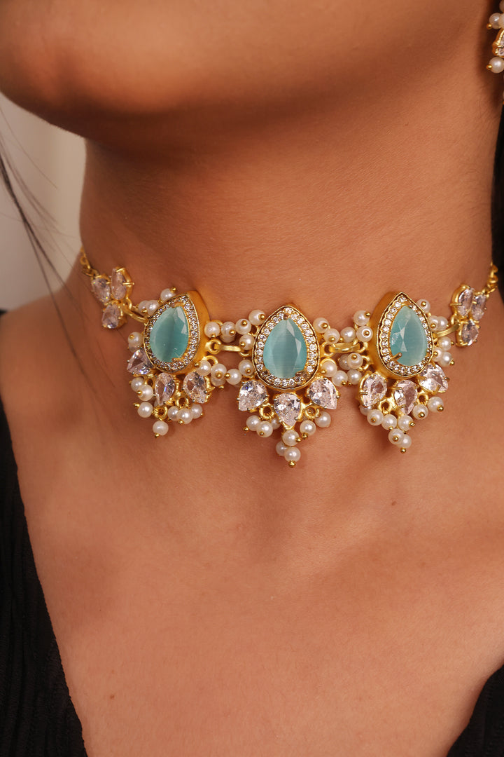 Close-up of a gold necklace with turquoise stones and pearl accents on a person wearing a black top.