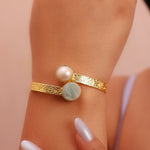 Load image into Gallery viewer, Gold bracelet with two round stones on a wrist against a pink background
