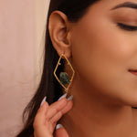 Load image into Gallery viewer, Close-up of a person wearing gold earrings with green gemstones against a neutral background
