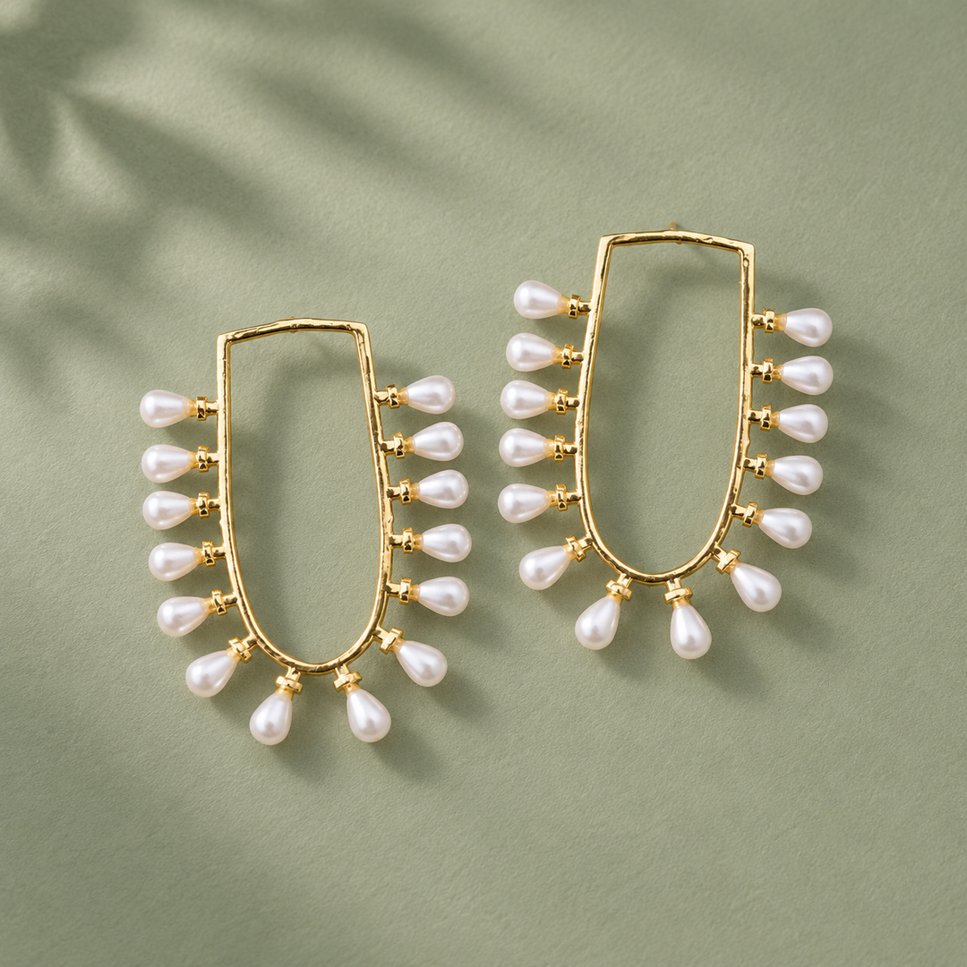 Pearl-fringed U-frame earrings arranged on a sage-green surface