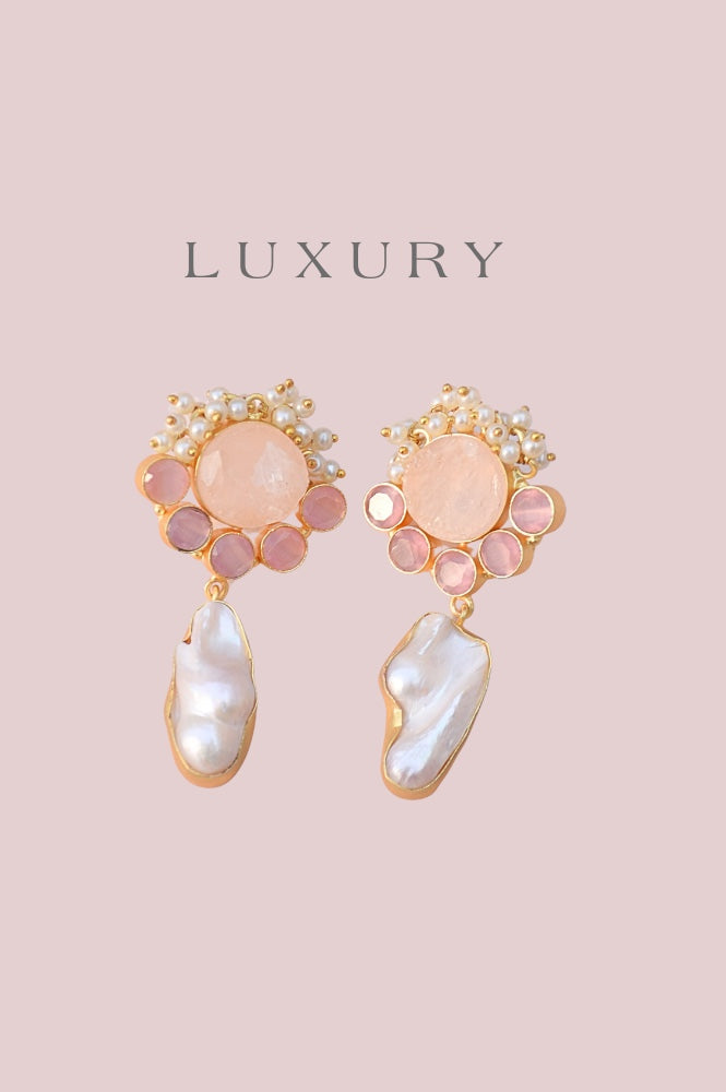 Gold and pink gemstone earrings with pearls and irregular white pearl drops, displayed on a pale pink background with the word LUXURY above them.